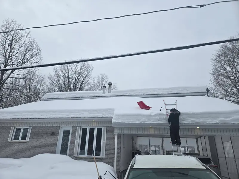 Travailleur dégageant la neige sur une toiture résidentielle